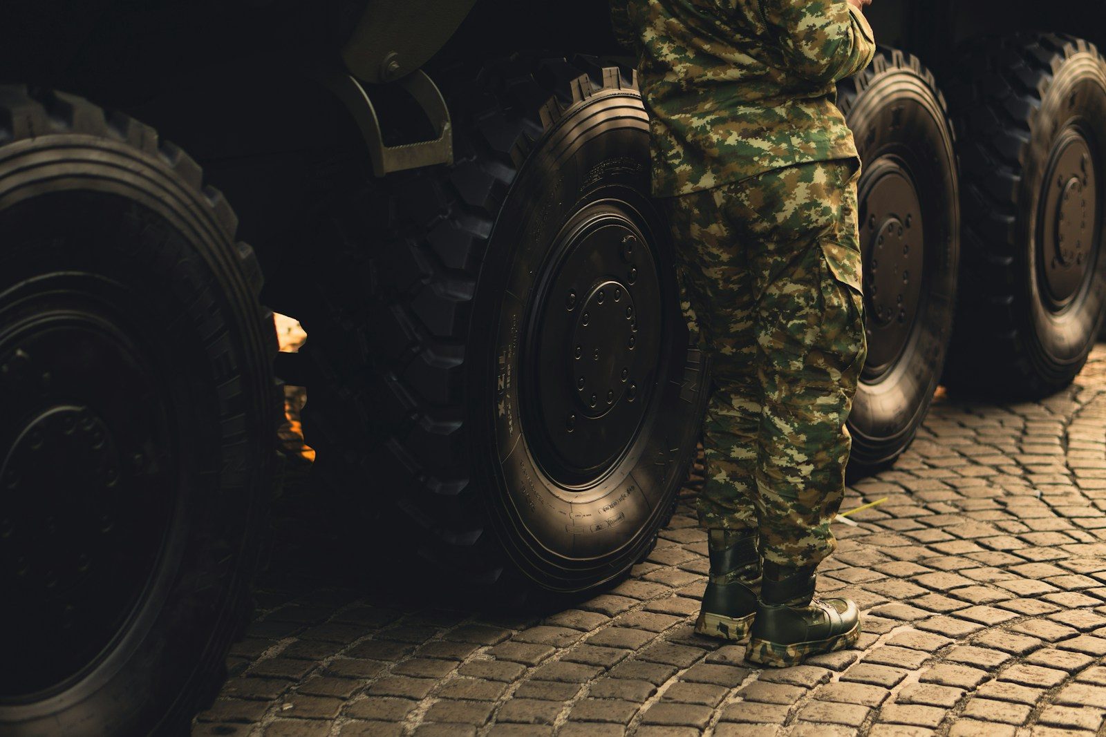 A man in camouflage standing next to a large truck